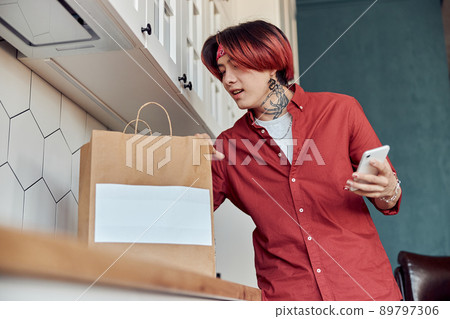 Stylish Asian guy holding phone while receiving food delivery at home 89797306