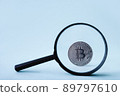 Bitcoin through a magnifying glass against the blue background. Digital payment system, cryptocurrency. Online currency and blockchain technology. Search for internet money.  89797610