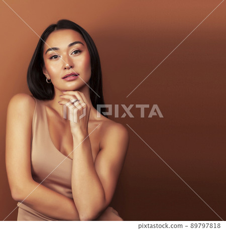 young pretty asian woman cheerful smiling posing on warm brown background, lifestyle people concept close up young pretty asian woman cheerful smiling posing on warm brown background, lifestyle people concept close up 89797818