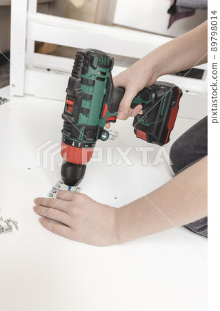 Young woman with cordless screwdriver assembling white folding table on the floor 89798014