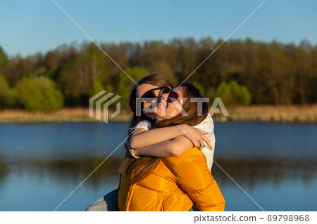 Playful mother giving daughter piggy back ride at spring lake shore. 89798968