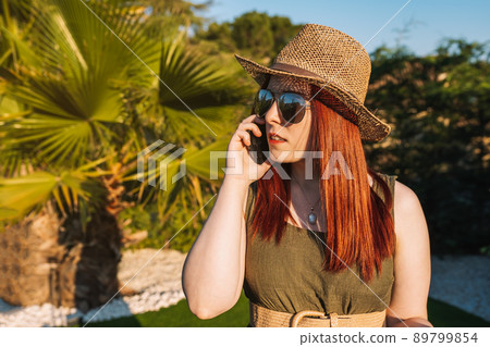 young red-haired woman travelling, calls her family on her mobile phone when she arrives at her holiday destination. young red-haired woman travelling, calls her family on her mobile phone when she arrives at her holiday destination. 89799854
