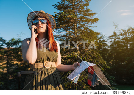 young red-haired girl calling with her smart phone for a taxi to pick her up at her resort. travel, summer holiday, 89799882