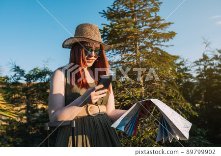 woman looking up the location of the hotel on her mobile phone when arriving at her travel destination. trip and leisure woman looking up the location of the hotel on her mobile phone when arriving at her travel destination. trip and leisure 89799902