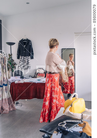 mature woman trying on handbags in front of mirror in fashion shop. blonde woman buying a large handbag. vertical mature woman trying on handbags in front of mirror in fashion shop. blonde woman buying a large handbag. vertical 89800079