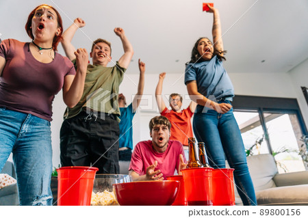 friends jumping for joy watching e-sports on TV after their team's victory. group of young watching soccer on tv. 89800156