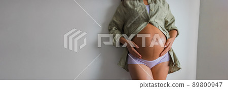 Pregnant woman banner. Pregnancy home lifestyle in underwear and organic cotton casual shirt belly on white wall background panoramic Pregnant woman banner. Pregnancy home lifestyle in underwear and organic cotton casual shirt belly on white wall background panoramic 89800947