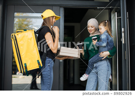 Arabic woman holding her daughter in arms, opens doors of her house and meets delivery woman Arabic woman holding her daughter in arms, opens doors of her house and meets delivery woman 89802926