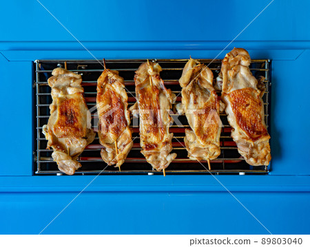 Grilled Chicken stick on the plain blue electric stove from the top view for simple and minimal food background 89803040