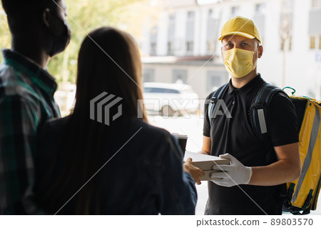 Smilling delivery man in yellow face mask, uniform cap delivering cardboard boxes with pizza Smilling delivery man in yellow face mask, uniform cap delivering cardboard boxes with pizza 89803570