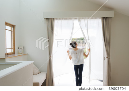 Woman opening the curtain at home Woman opening the curtain at home 89803704