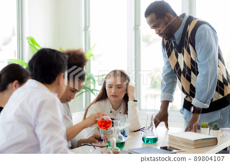 Young teacher teaching group student about science and test chemical for liquid in the lab of school 89804107