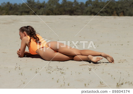 Fit woman in swimsuit sunbathing on sandy beach Fit woman in swimsuit sunbathing on sandy beach 89804374