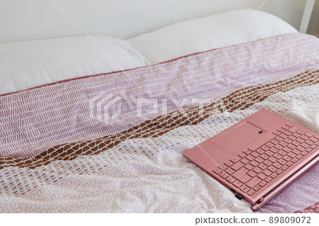 Pink laptop placed on a double-sized duvet Pink laptop placed on a double-sized duvet 89809072