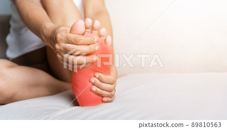 Asian woman sitting on sofa feeling pain in her foot at home 89810563