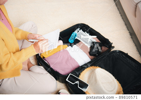 Woman writing paper take note and packing suitcase to vacation writing paper list sitting on room Woman writing paper take note and packing suitcase to vacation writing paper list sitting on room 89810571