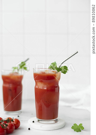 two glasses of tomato juice with a sprig of parsley and pepper on a white table two glasses of tomato juice with a sprig of parsley and pepper on a white table 89810862