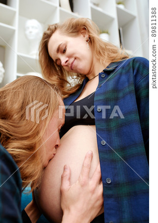 Close up of a happy man kissing the belly of his lovely pregnant wife standing in the white bedroom. Dad waits the birth of the baby. Sensual photo. Close up of a happy man kissing the belly of his lovely pregnant wife standing in the white bedroom. Dad waits the birth of the baby. Sensual photo. 89811388