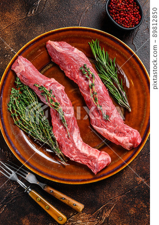 Raw flank beef meat steak on a plate. Dark background. Top view 89812850