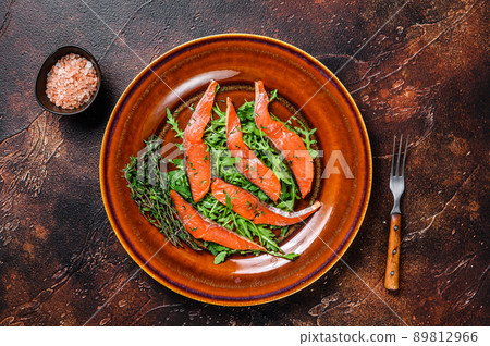 Salad with arugula and smoked salmon fillet slices. Dark background. Top view Salad with arugula and smoked salmon fillet slices. Dark background. Top view 89812966
