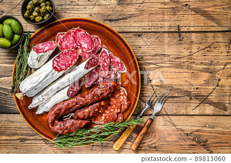Spanish charcuterie with sliced sausages salami, fuet and chorizo on a rustic plate. wooden background. Top view. Copy space 89813060