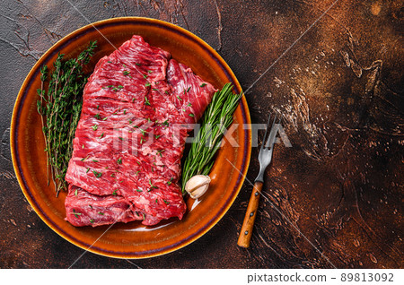 Raw beef skirt meat steak on a rustic plate with herbs. Dark background. Top view. Copy space 89813092