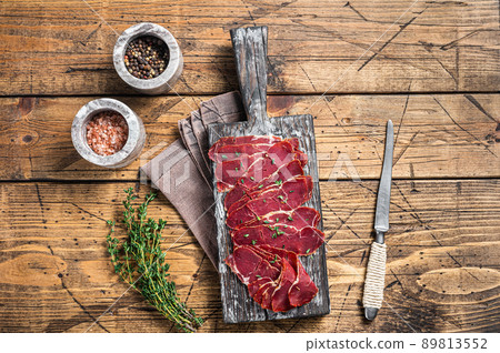 Dried Pastrami slices, beef meat with herbs on wooden board. Wooden background. Top view 89813552