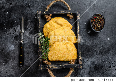 Raw chicken cordon bleu meat cutlets in a wooden tray with herbs. Black background. Top view 89813553
