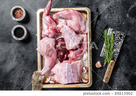 Raw wild hare slices legs, fresh game meat in steel tray with herb. Black background. Top view Raw wild hare slices legs, fresh game meat in steel tray with herb. Black background. Top view 89813902