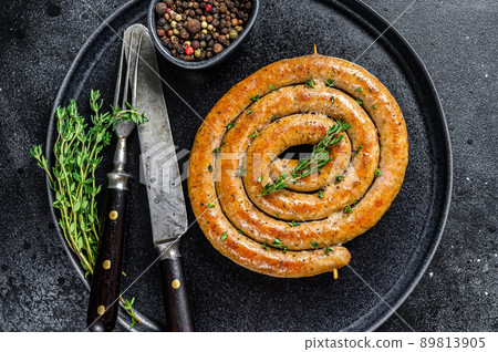 Roasted spicy spiral meat sausage on a plate. Black background. Top view 89813905