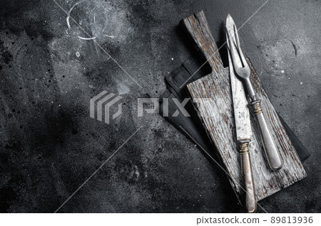 Vintage butcher meat fork and knife with cloth towel on wooden table. Black background. Top view. Copy space Vintage butcher meat fork and knife with cloth towel on wooden table. Black background. Top view. Copy space 89813936