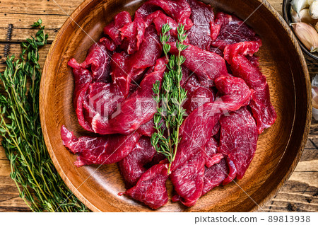 Raw uncooked beef meat sliced in strips with fresh herbs for beef stroganoff. wooden background. Top view Raw uncooked beef meat sliced in strips with fresh herbs for beef stroganoff. wooden background. Top view 89813938