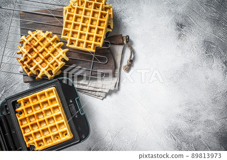 Cooking of fresh waffles in waffle maker. White background. Top view. Copy space 89813973
