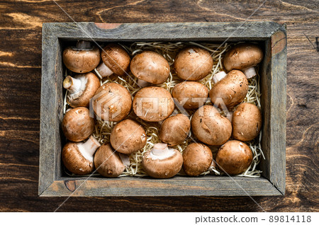 Raw Fresh champignon mushrooms in a wooden box. Dark background. Top view 89814118