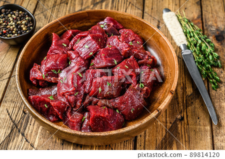 Raw cut wild venison meat for a goulash in a wooden plate. Wooden background. Top view 89814120