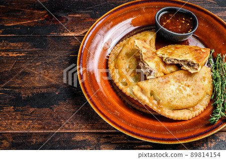 Fried empanadas with minced beef meat served on a plate with chili sauce. Dark Wooden background. Top view. Copy space Fried empanadas with minced beef meat served on a plate with chili sauce. Dark Wooden background. Top view. Copy space 89814154