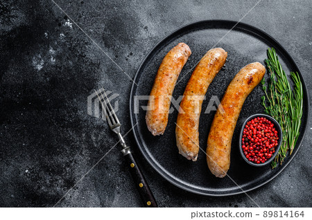 Sausages fried with spices and herbs on a plate. Top view. Black background. Copy space 89814164
