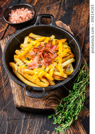 French fries with melted mix of cheddar cheese and bacon served in a pan. Dark wooden background. Top view 89814165