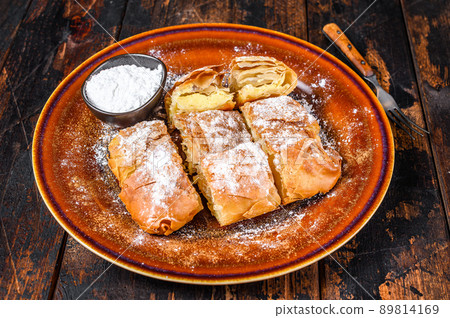 Sliced Greek Bougatsa pie with phyllo dough and semolina custard cream. Dark Wooden background. Top view Sliced Greek Bougatsa pie with phyllo dough and semolina custard cream. Dark Wooden background. Top view 89814169