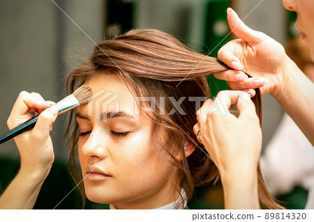 Makeup artist and hairdresser prepare the bride making hairstyle and makeup in a beauty salon Makeup artist and hairdresser prepare the bride making hairstyle and makeup in a beauty salon 89814320
