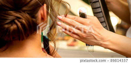 Professional hairdresser styling and fixing with hairspray long woman curly hair in a beauty salon 89814337