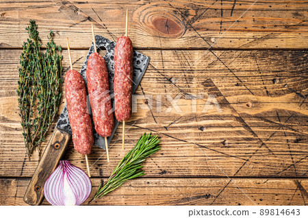 Fresh Raw kofta or lula kebabs skewers on a butcher cleaver with herbs. wooden background. Top view. Copy space Fresh Raw kofta or lula kebabs skewers on a butcher cleaver with herbs. wooden background. Top view. Copy space 89814643