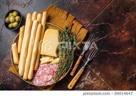 Appetizer plate with antipasti snacks grissini bread sticks, salami, olives and parmesan cheese. Dark bakground. Top view. Copy space Appetizer plate with antipasti snacks grissini bread sticks, salami, olives and parmesan cheese. Dark bakground. Top view. Copy space 89814647