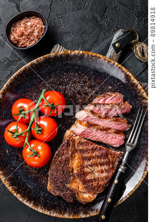 Grilled rib eye steak, ribeye beef marbled meat on a plate with tomato. Black background. top view 89814918