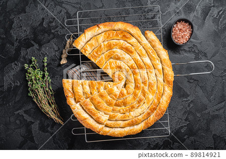 Turkish Tepsi Boregi, Round Borek cheese pie on kitchen board. Black background. Top view 89814921