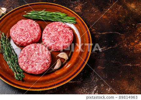 Raw burger meat cutlets with mince beef and herbs on a plate. Dark background. Top view. Copy space Raw burger meat cutlets with mince beef and herbs on a plate. Dark background. Top view. Copy space 89814963