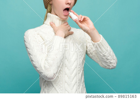 Sick young woman in scarf t use spray isolated on blue background Sick young woman in scarf t use spray isolated on blue background 89815163