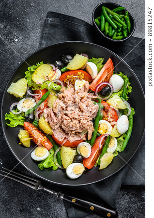 Tuna salad nicoise with vegetables, eggs and anchovies in a plate. Black background. top view 89815247