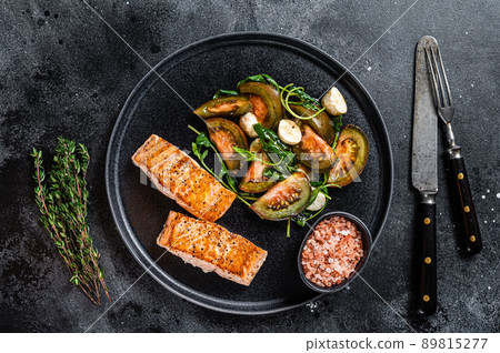 Fish meal with Roasted Salmon Fillet Steaks and arugula tomato salad on a plate. Black background. Top view Fish meal with Roasted Salmon Fillet Steaks and arugula tomato salad on a plate. Black background. Top view 89815277