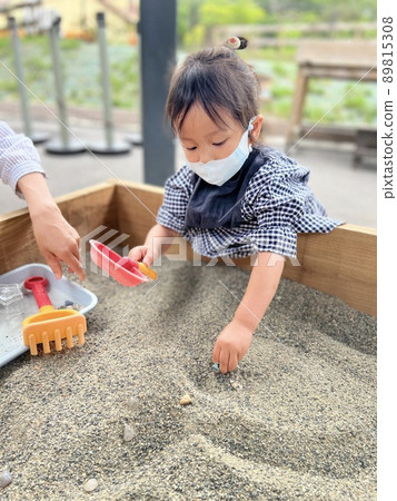 Girl wearing a mask and playing in the sandbox 89815308